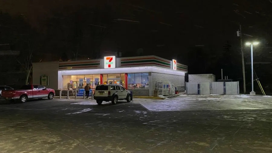 A convenience store lit up at night, empty parking lot in front
